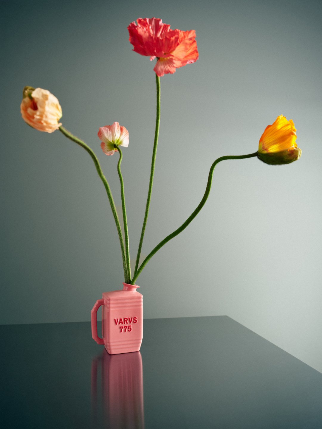 Red and yellow flowers arranged in pink bottle on reflective surface, Varus 775 by Olssøn Barbieri, Lübbecke, Olssøn Barbieri / Varus Brennerei, Lübbecke, Germany