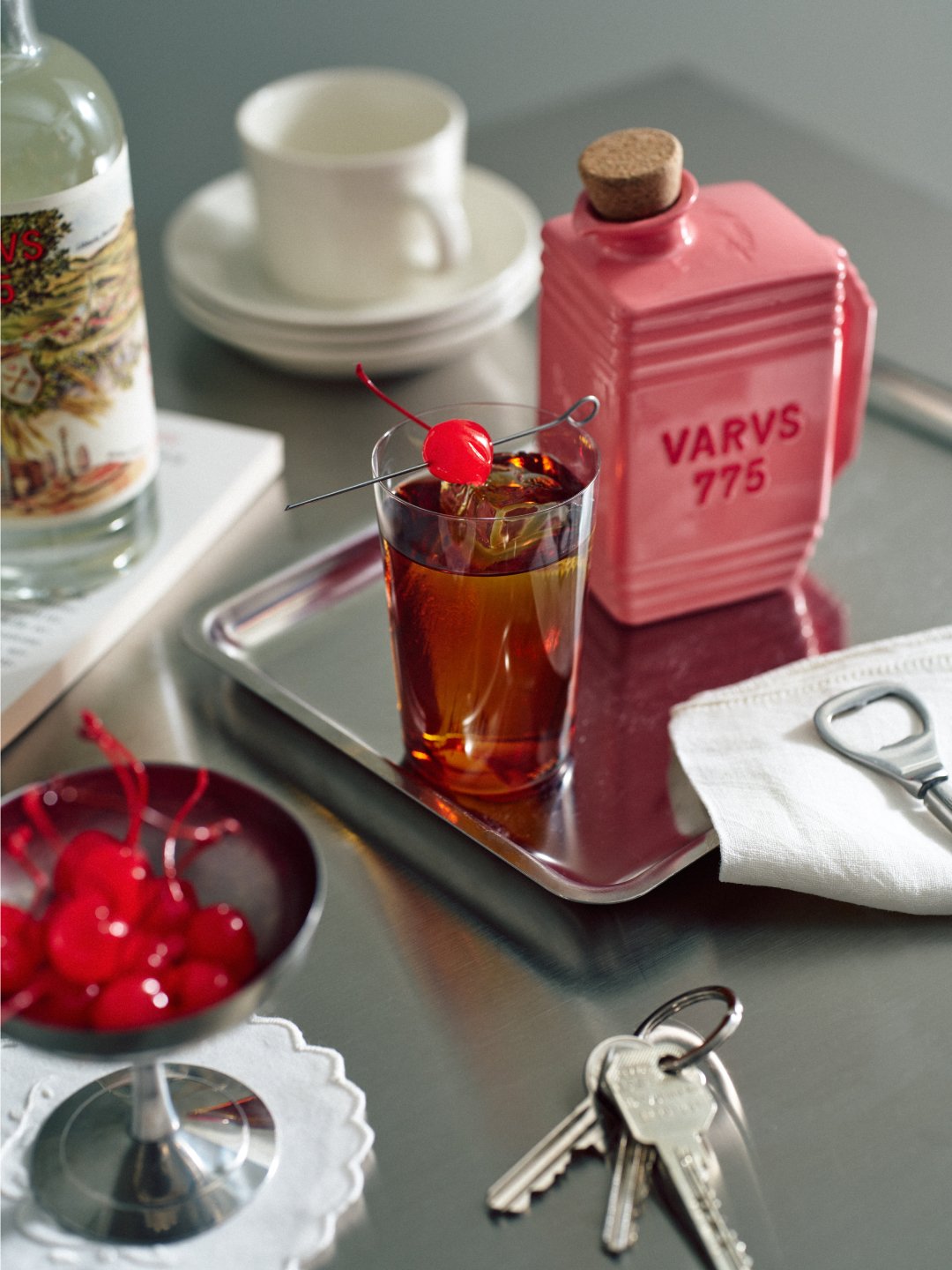 Pink bottle beside drink glass and keys on reflective tabletop, Varus 775 by Olssøn Barbieri, Lübbecke, Olssøn Barbieri / Varus Brennerei, Lübbecke, Germany