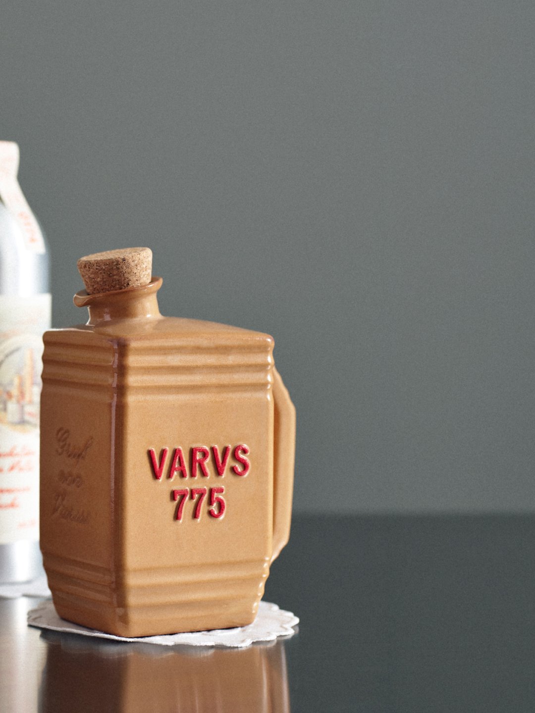 Tan ribbed bottle reflected on tabletop against softly lit gray backdrop, Varus 775 by Olssøn Barbieri, Lübbecke, Olssøn Barbieri / Varus Brennerei, Lübbecke, Germany