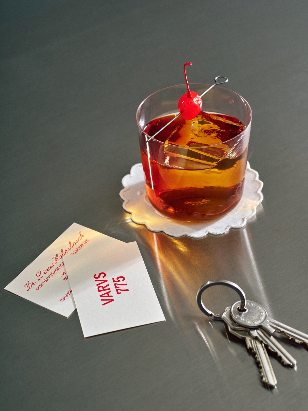 Overhead still life of amber drink with keys and paper cards, Varus 775 by Olssøn Barbieri, Lübbecke, Olssøn Barbieri / Varus Brennerei, Lübbecke, Germany